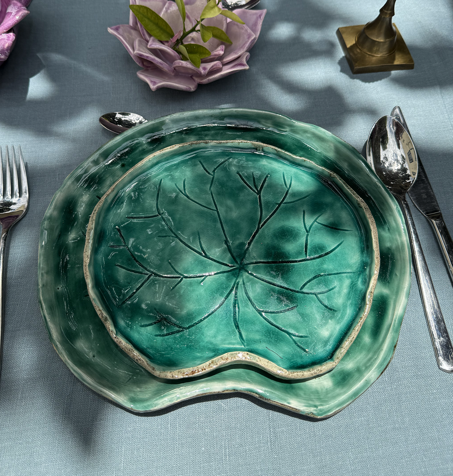 Vajilla de cerámica con platos y bowl en forma de la flor y las hojas, simulando un jardín de nenúfares flotantes en la mesa.