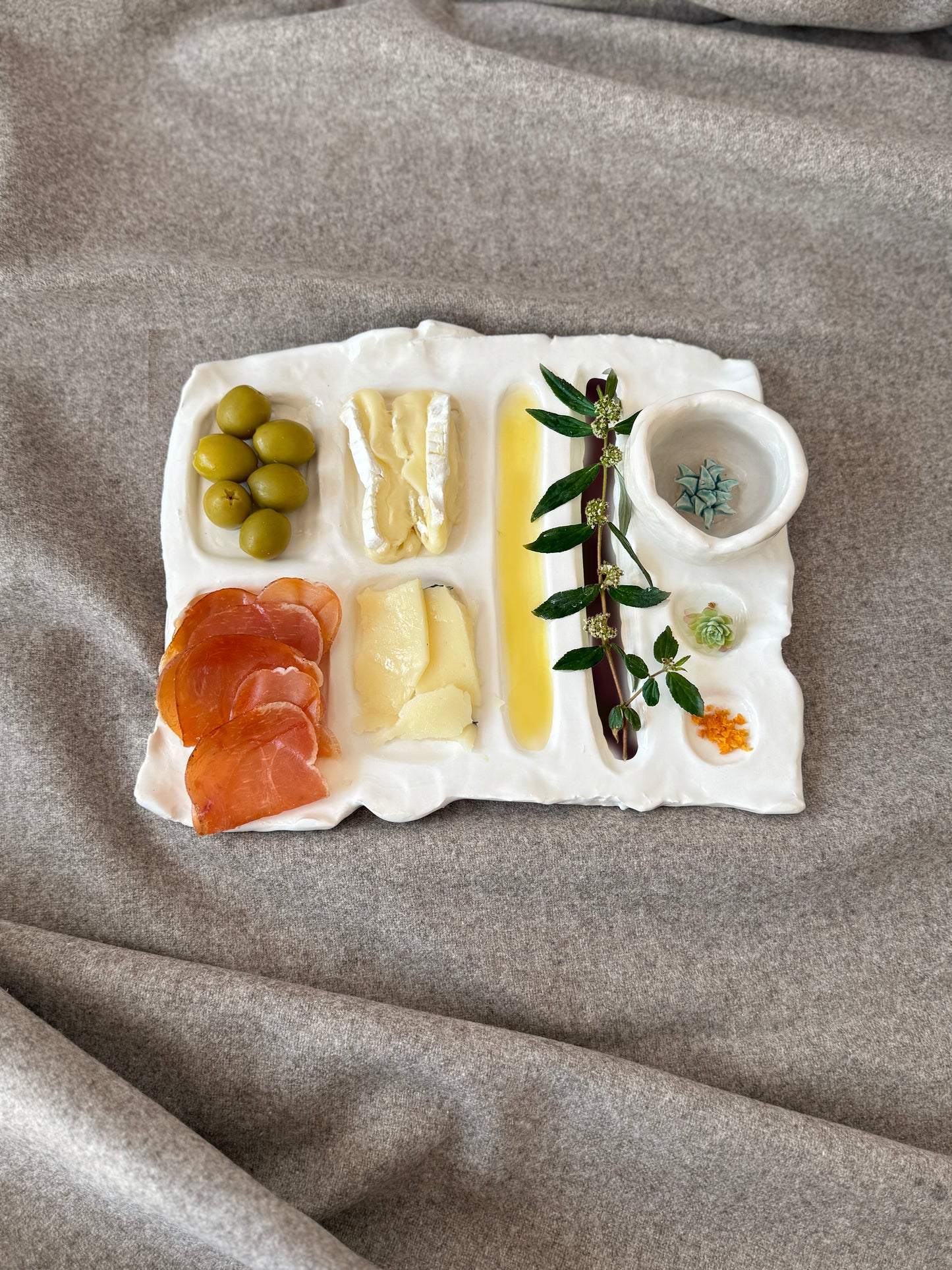 tabla de cerámica artesanal, diseñada para resaltar la presentación de tus aperitivos favoritos. Hecha a mano, forma orgánica y texturas naturales. Diseño con compartimentos para quesos, embutidos, aceitunas y salsas.Incluye mezcalero de cerámica.