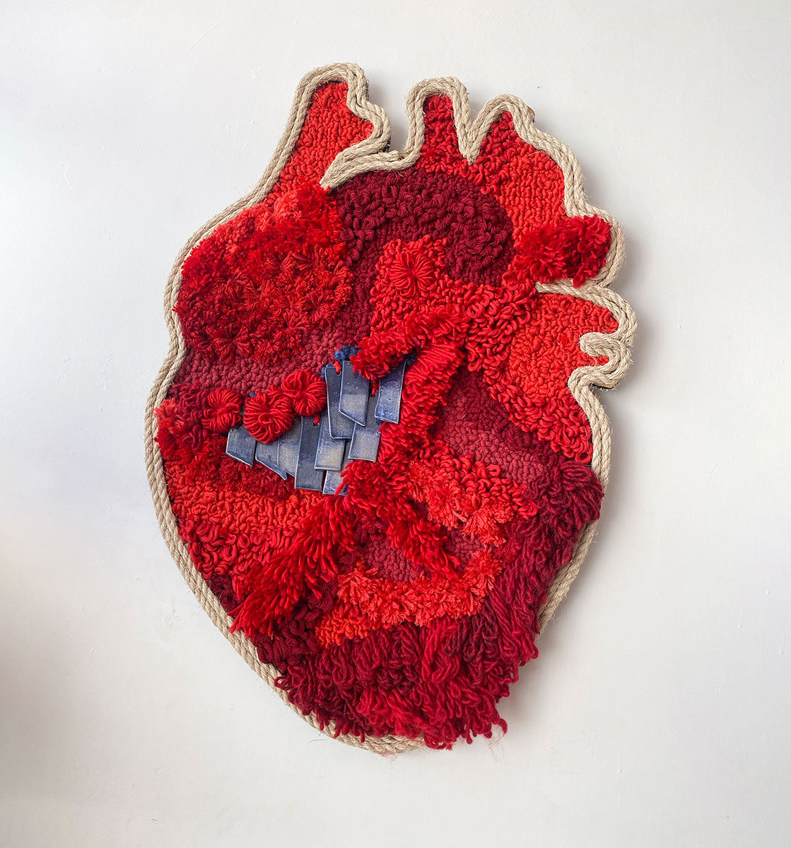 Arte textil en forma de corazón, confeccionado en tonos rojos vibrantes, destacando una variedad de texturas y patrones intrincados