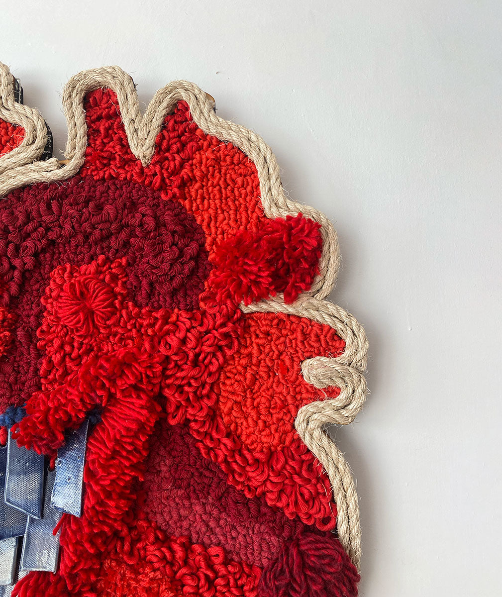 Arte textil en forma de corazón, confeccionado en tonos rojos vibrantes, destacando una variedad de texturas y patrones intrincados