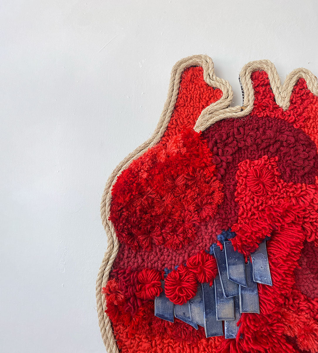 Arte textil en forma de corazón, confeccionado en tonos rojos vibrantes, destacando una variedad de texturas y patrones intrincados